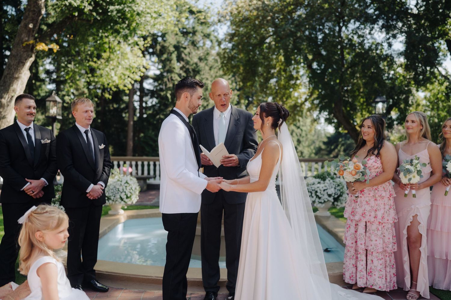 Outdoor wedding ceremony taking place in a beautiful garden setting with formal attire.