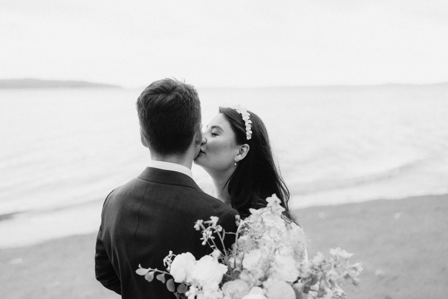 Romantic black and white wedding portrait on a cloudy day by the water.