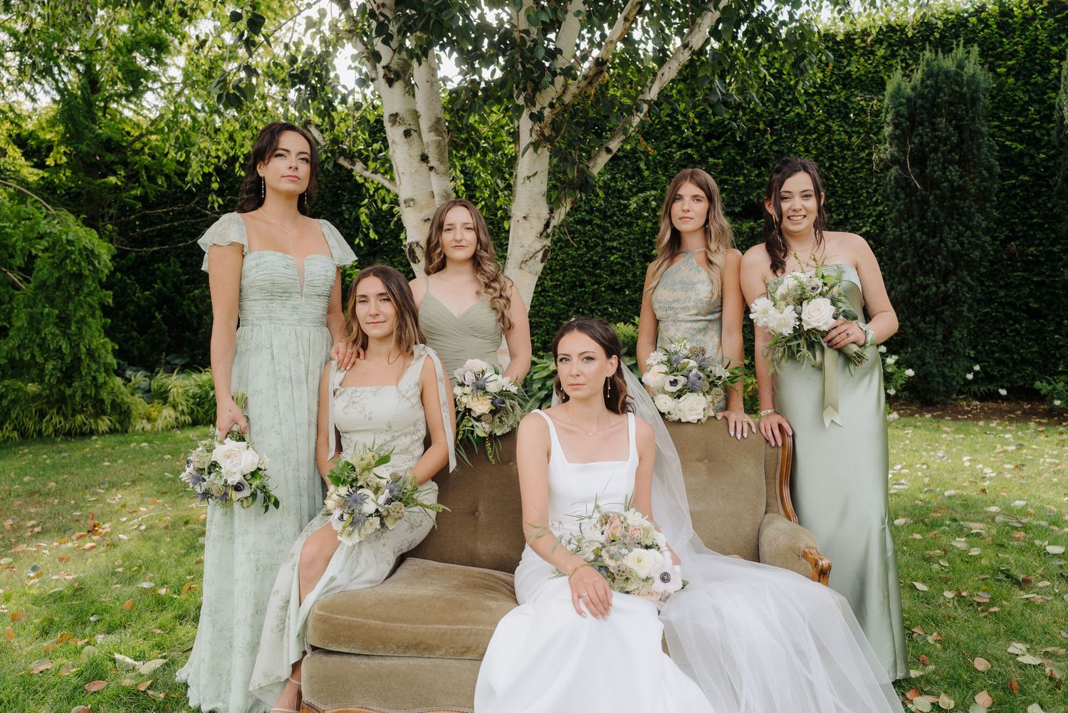 Wedding party in sage green bridesmaid dresses posing in a garden setting.