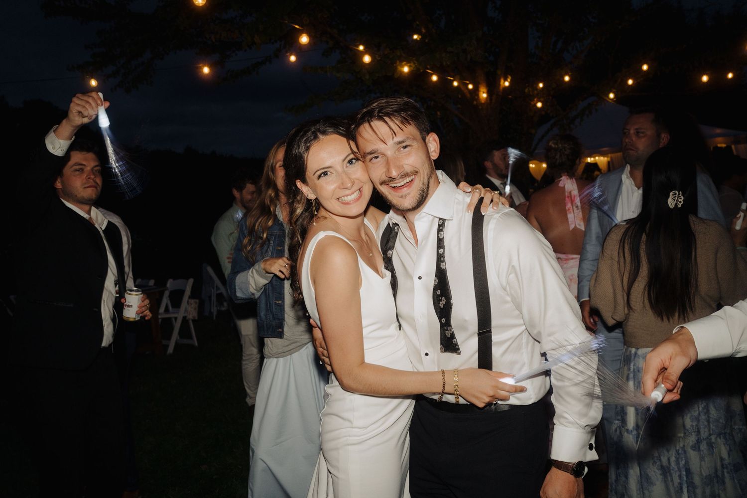 Wedding guests dancing and celebrating at an evening outdoor reception with string lights.