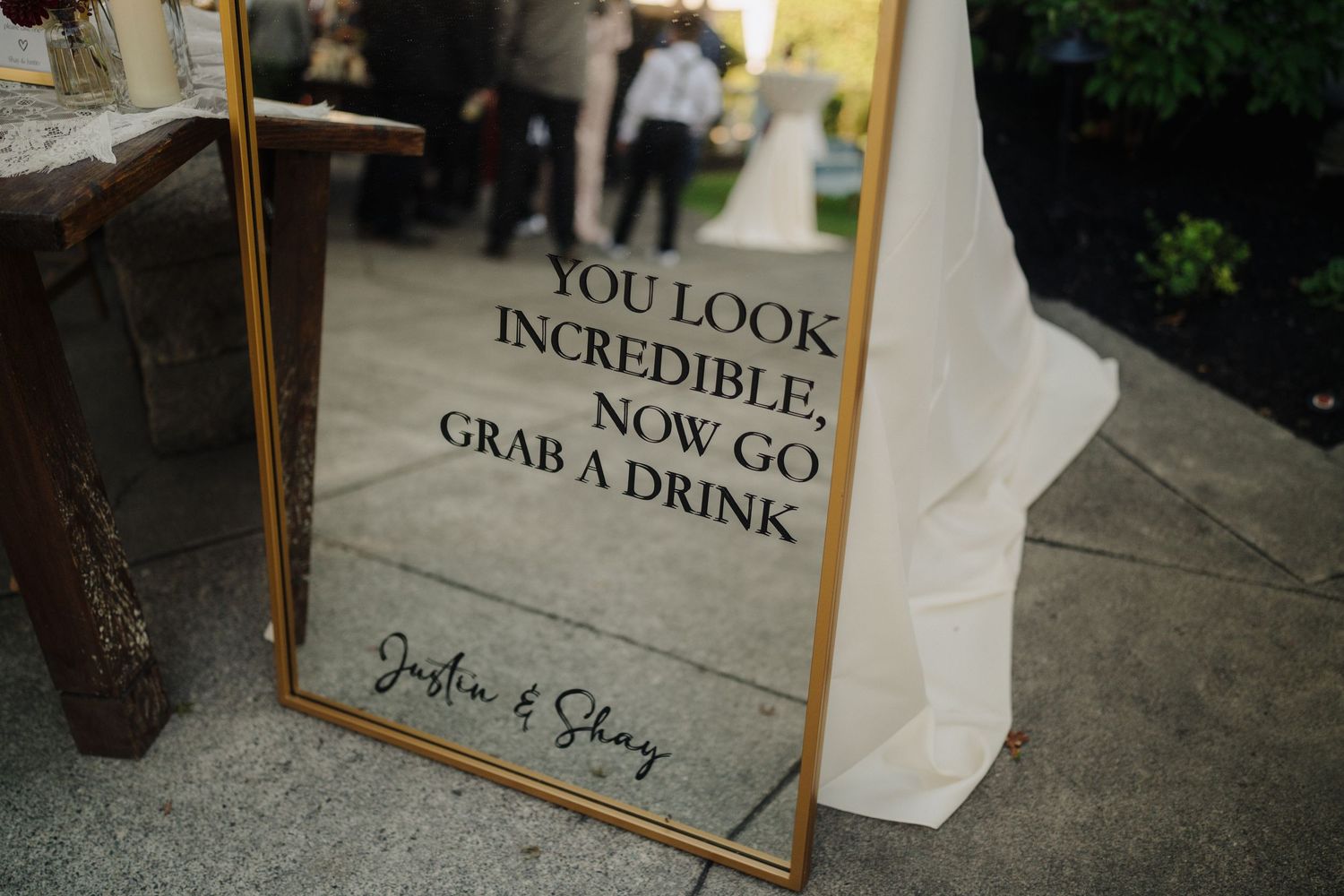 Gold-framed wedding sign reading 'You look incredible, now go grab a drink' against stone background.