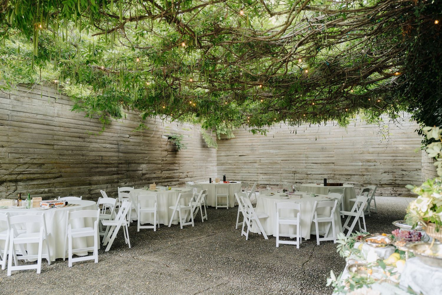 White folding chairs arranged under trees at an outdoor wedding venue with natural lighting.