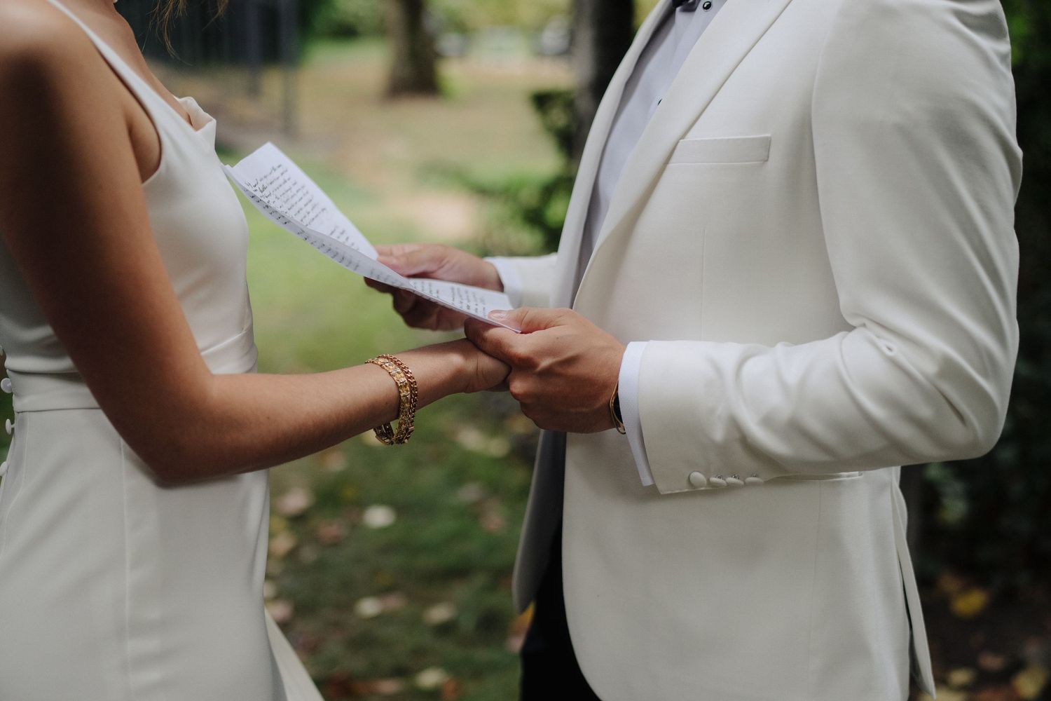 Close-up of hands exchanging wedding vows during an outdoor ceremony.