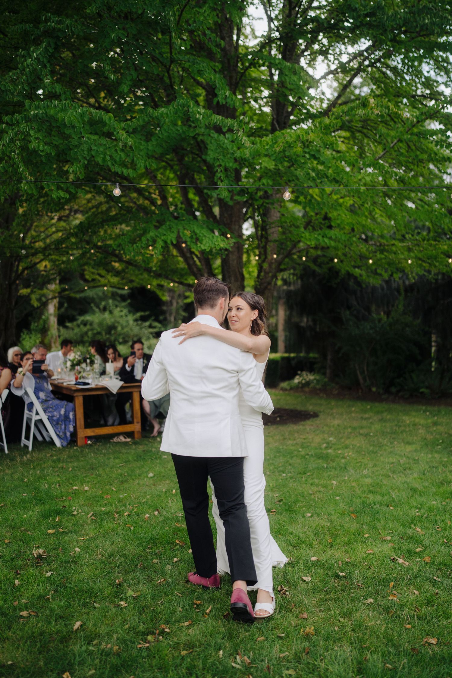 A couple shares a romantic dance moment on a lush green lawn during their wedding celebration.