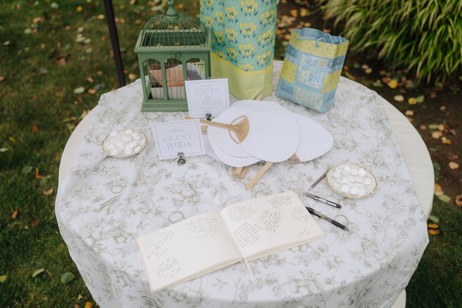 Wedding reception table setup with white lace tablecloth and decorative items in an outdoor garden setting.