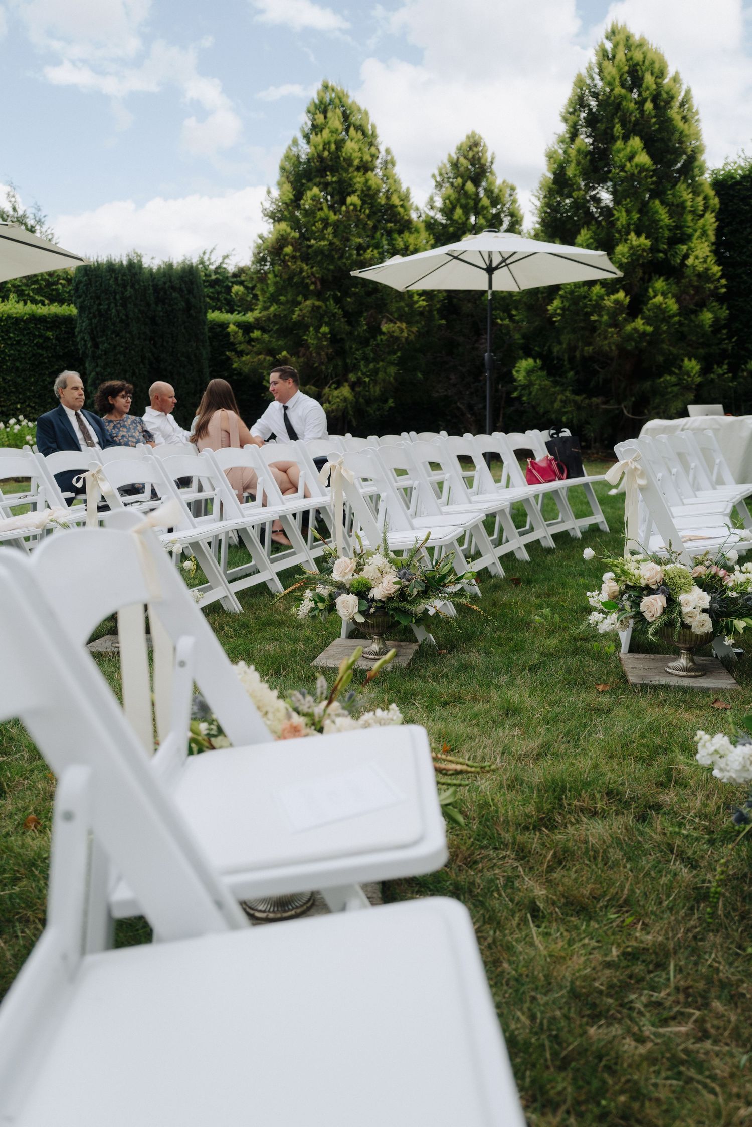 White folding chairs arranged in rows on a grassy lawn for an outdoor wedding ceremony with floral decorations.