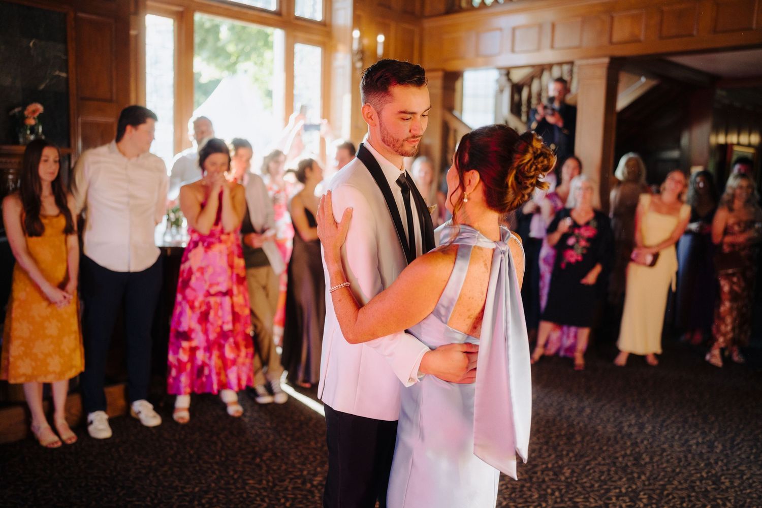 Wedding reception guests dancing and celebrating on a wooden dance floor under warm lighting.