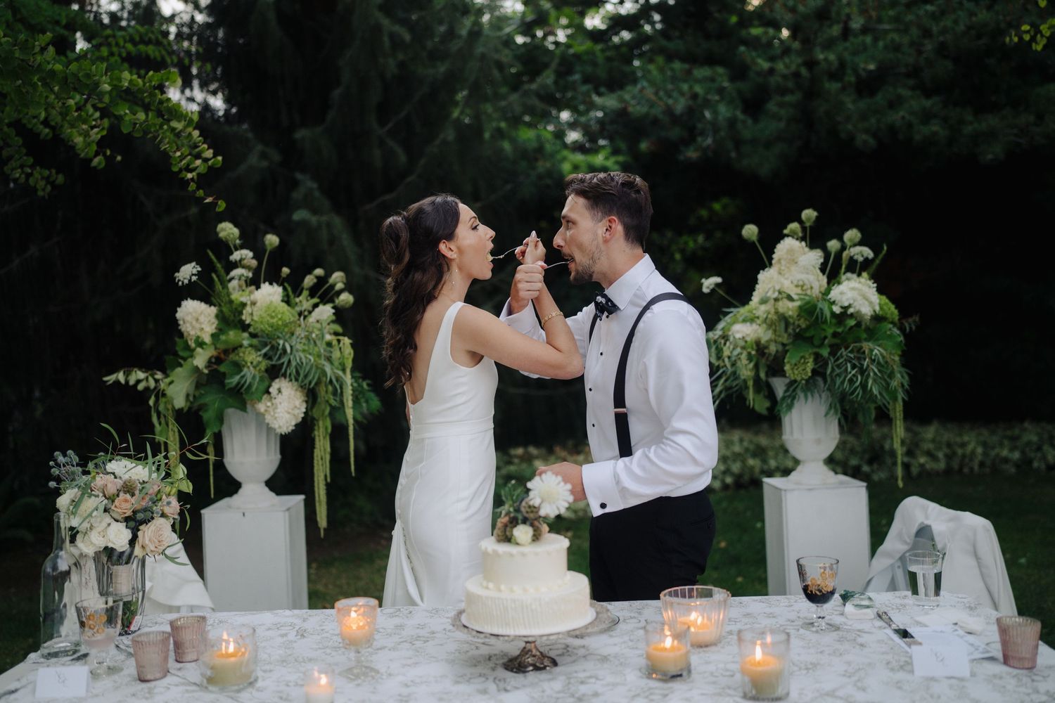 Romantic wedding table setup with candles and floral arrangements in an outdoor garden setting.