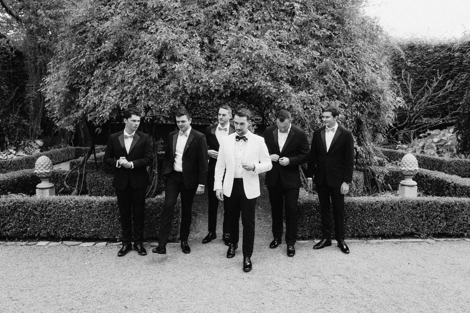 Black and white photo of groomsmen lined up against a garden backdrop.
