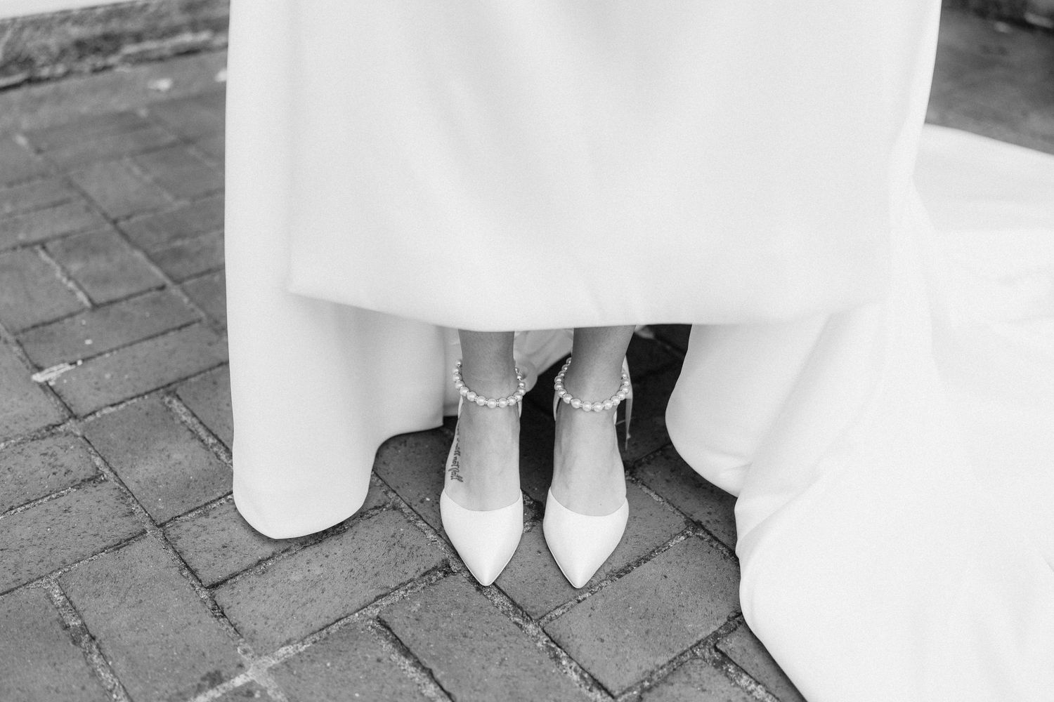 Row of white pointed-toe wedding shoes lined up on stone pavers outdoors.