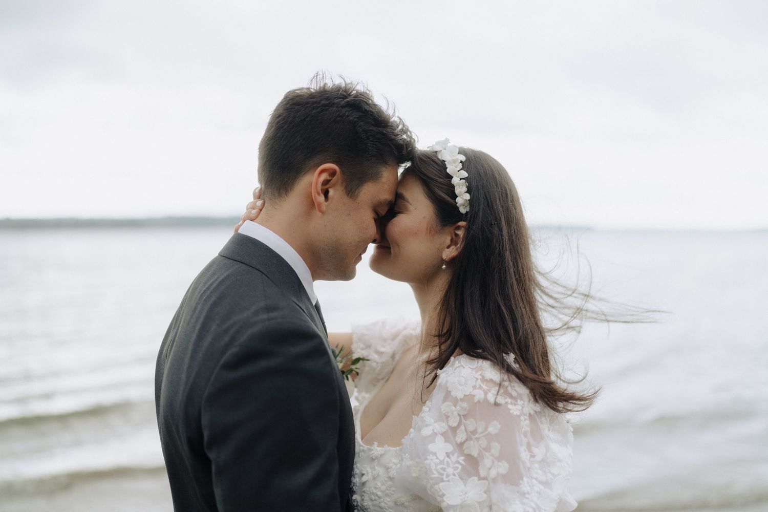 Romantic seaside moment between newlyweds with waves and cloudy sky in background.