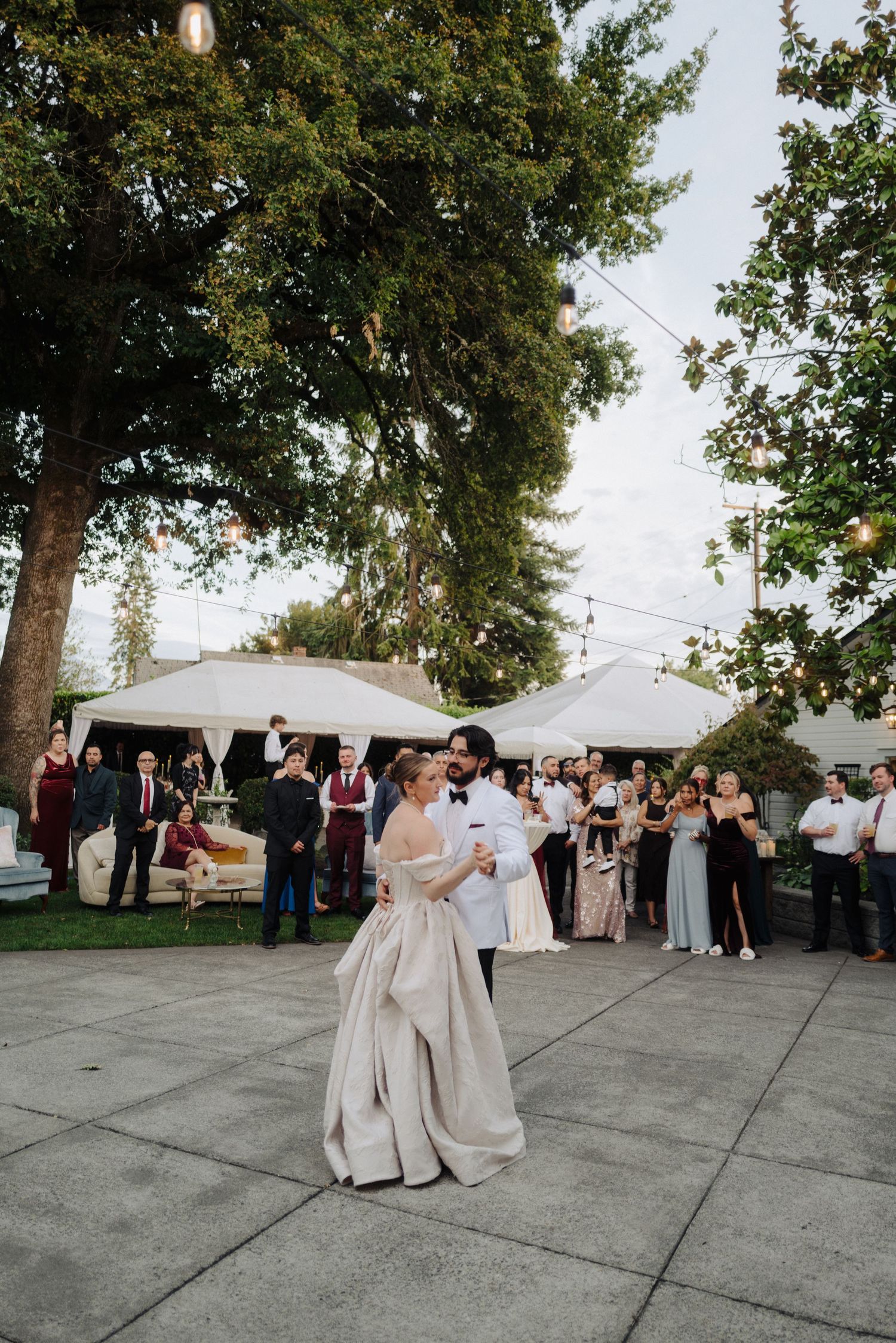 Elegant outdoor wedding reception with white tents and dancing couple in formal attire.