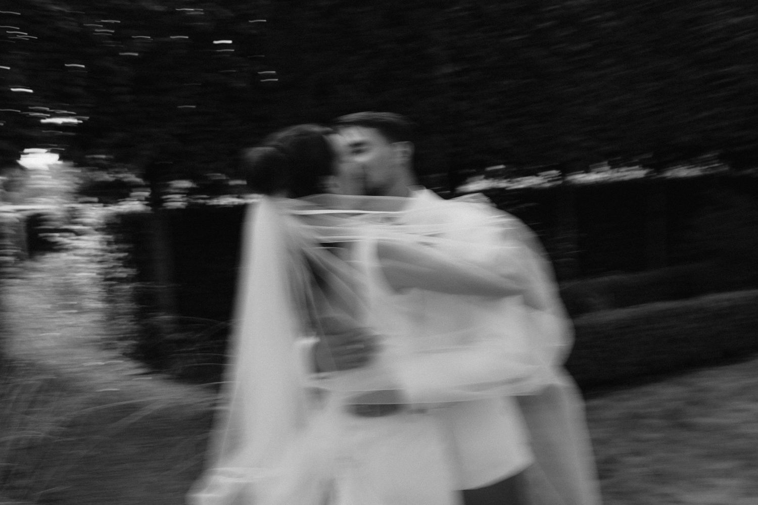 A black and white artistic wedding photo capturing a romantic moment in a garden setting.