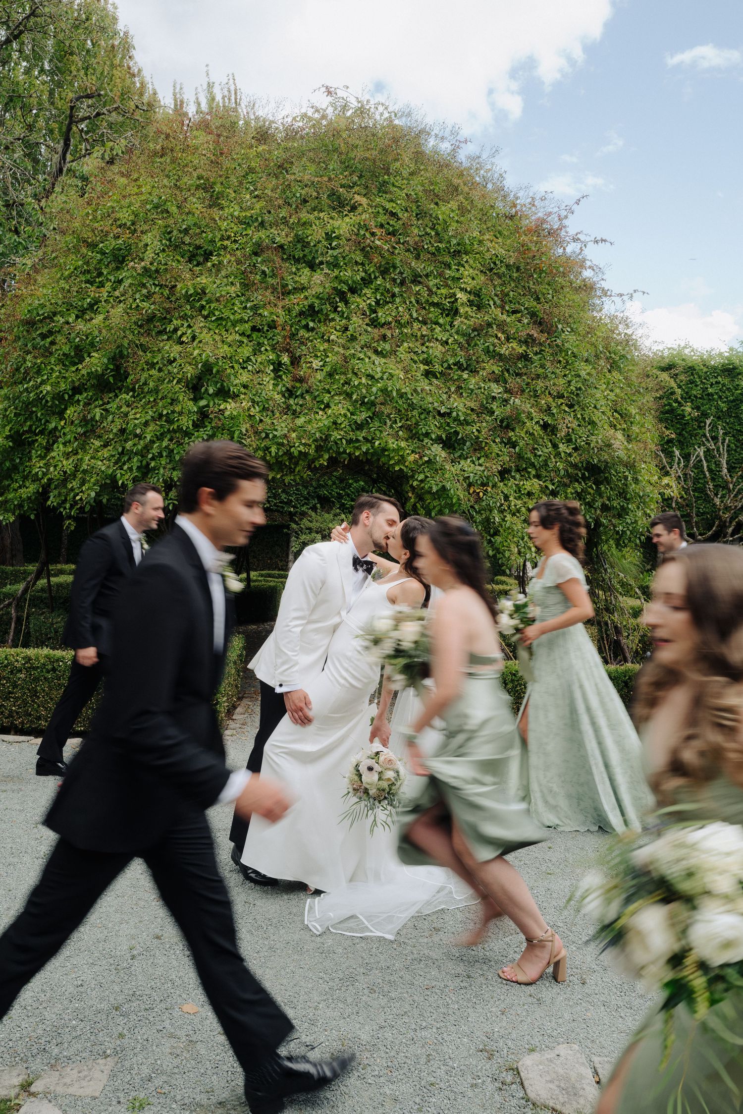 Wedding party runs playfully down a garden path in a candid motion-blur sequence.