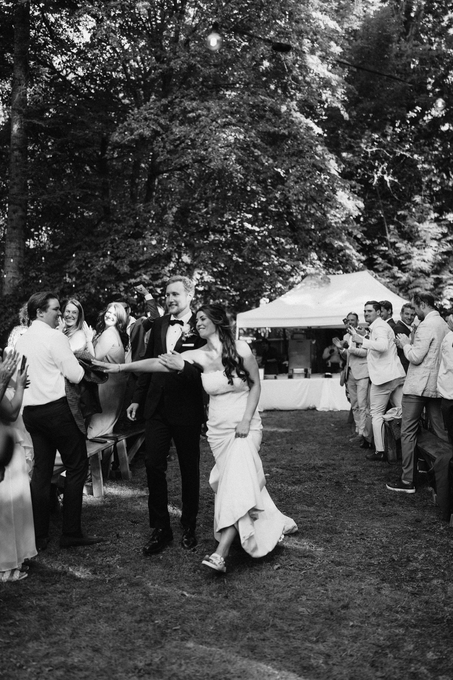 Black and white photo of wedding guests dancing and celebrating outdoors.