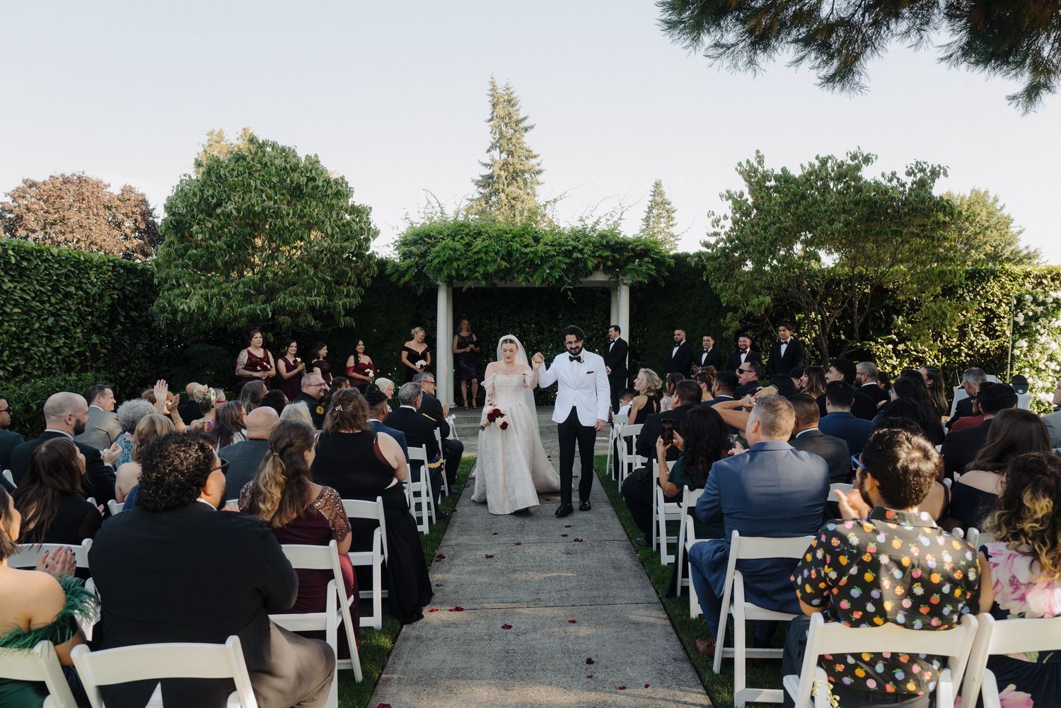 Outdoor wedding ceremony setup with white chairs arranged in rows under trees at sunset.