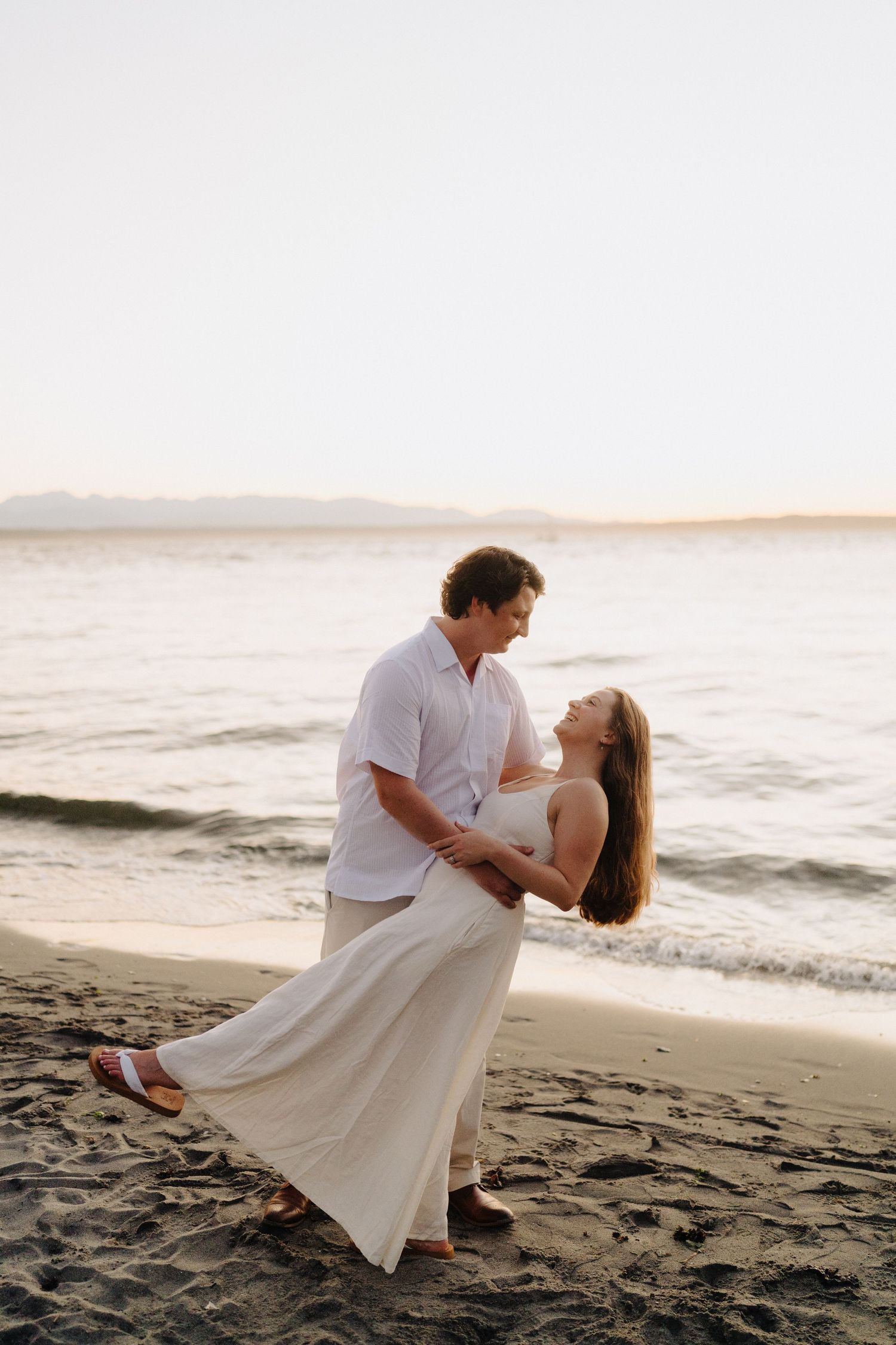 A romantic couple dances and embraces on a sandy beach during golden hour.