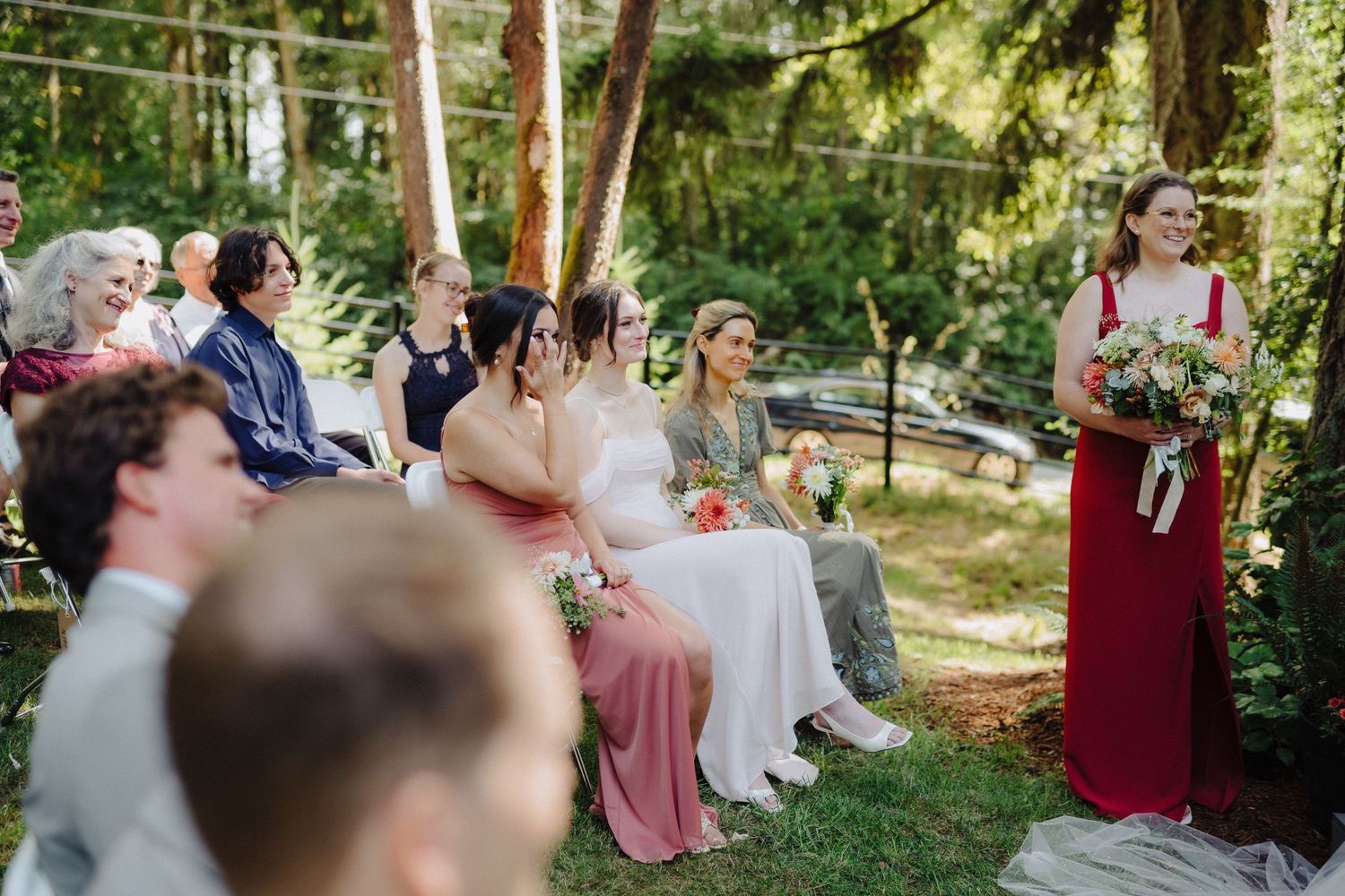 Wedding guests seated in rows outdoors beneath towering pine trees during a forest ceremony.