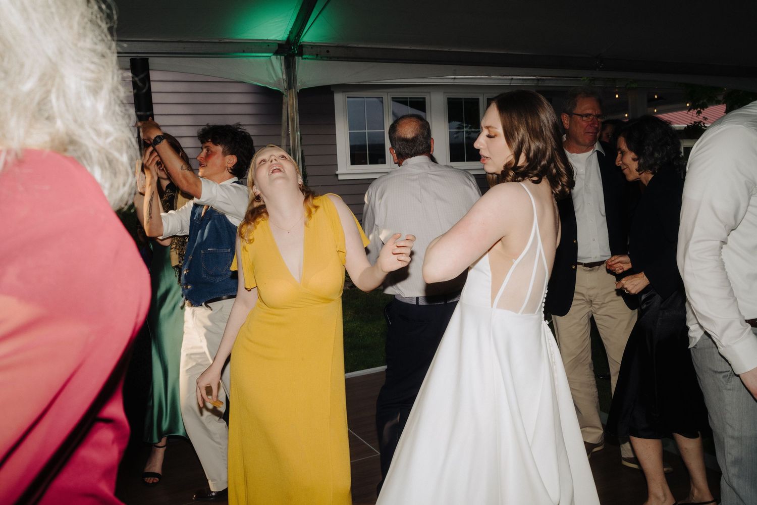 Wedding reception dance party under green lighting with guests in formal attire.