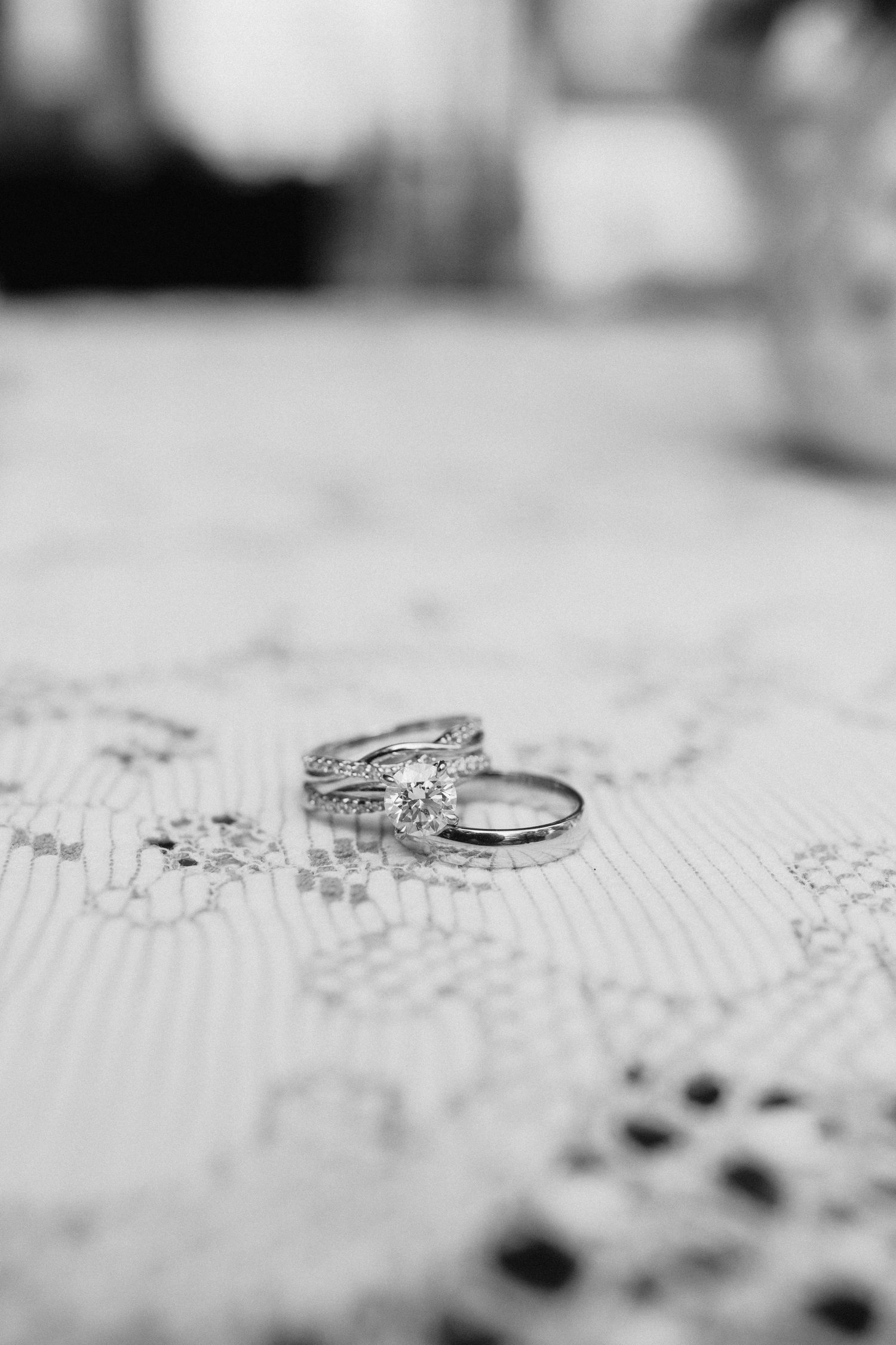 Close-up macro shots of elegant diamond engagement rings and wedding bands on textured white surface.