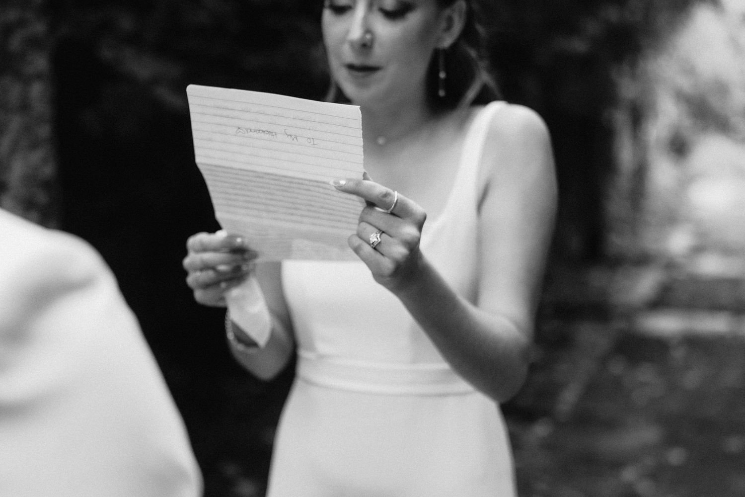 Black and white image showing person in elegant dress reading from paper during ceremony.
