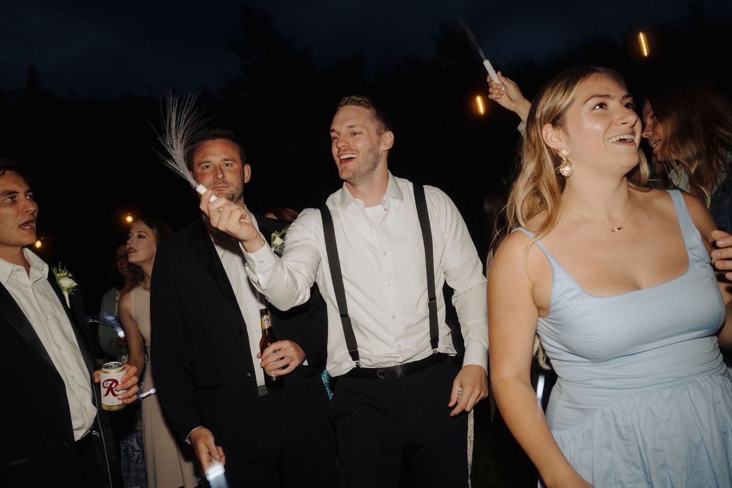 Wedding party guests dancing and celebrating at a nighttime reception under ambient lighting.