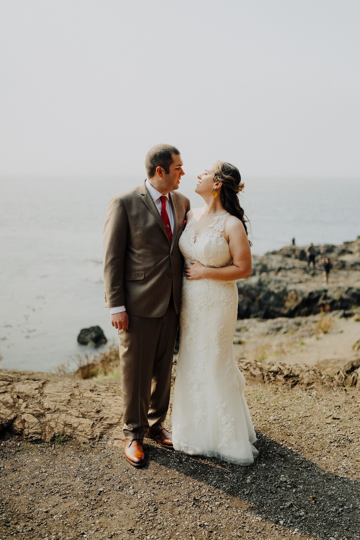 Newlyweds share an intimate moment on a coastal cliff during their wedding photoshoot.