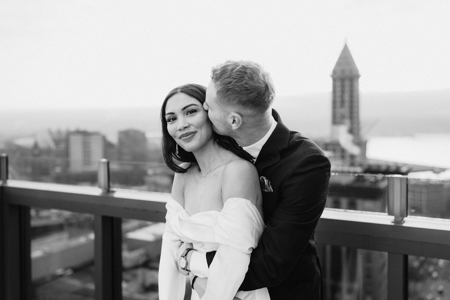 Elegant wedding couple sharing romantic moment on rooftop with scenic city view.