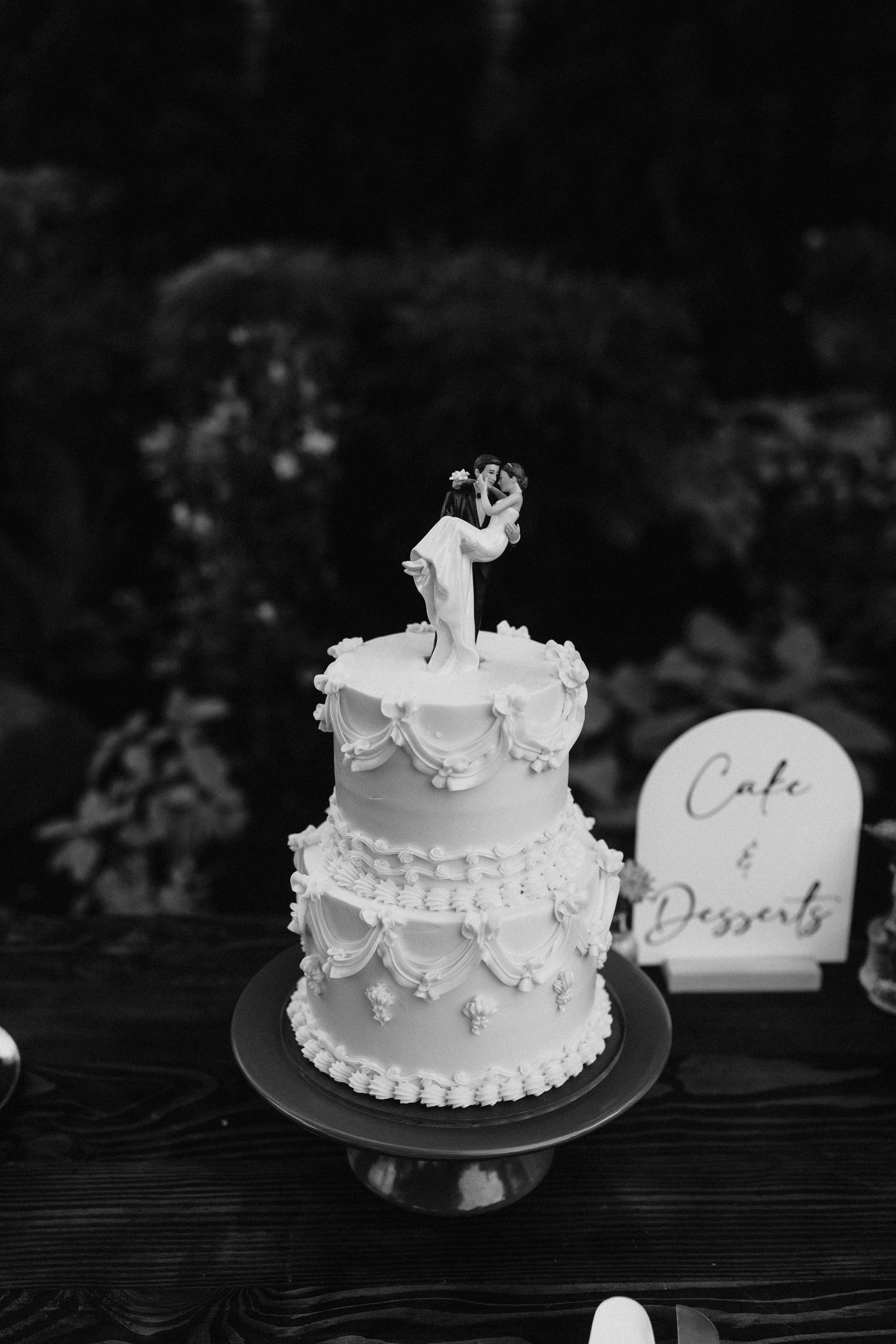 A classic white two-tier wedding cake with lace details and topper.