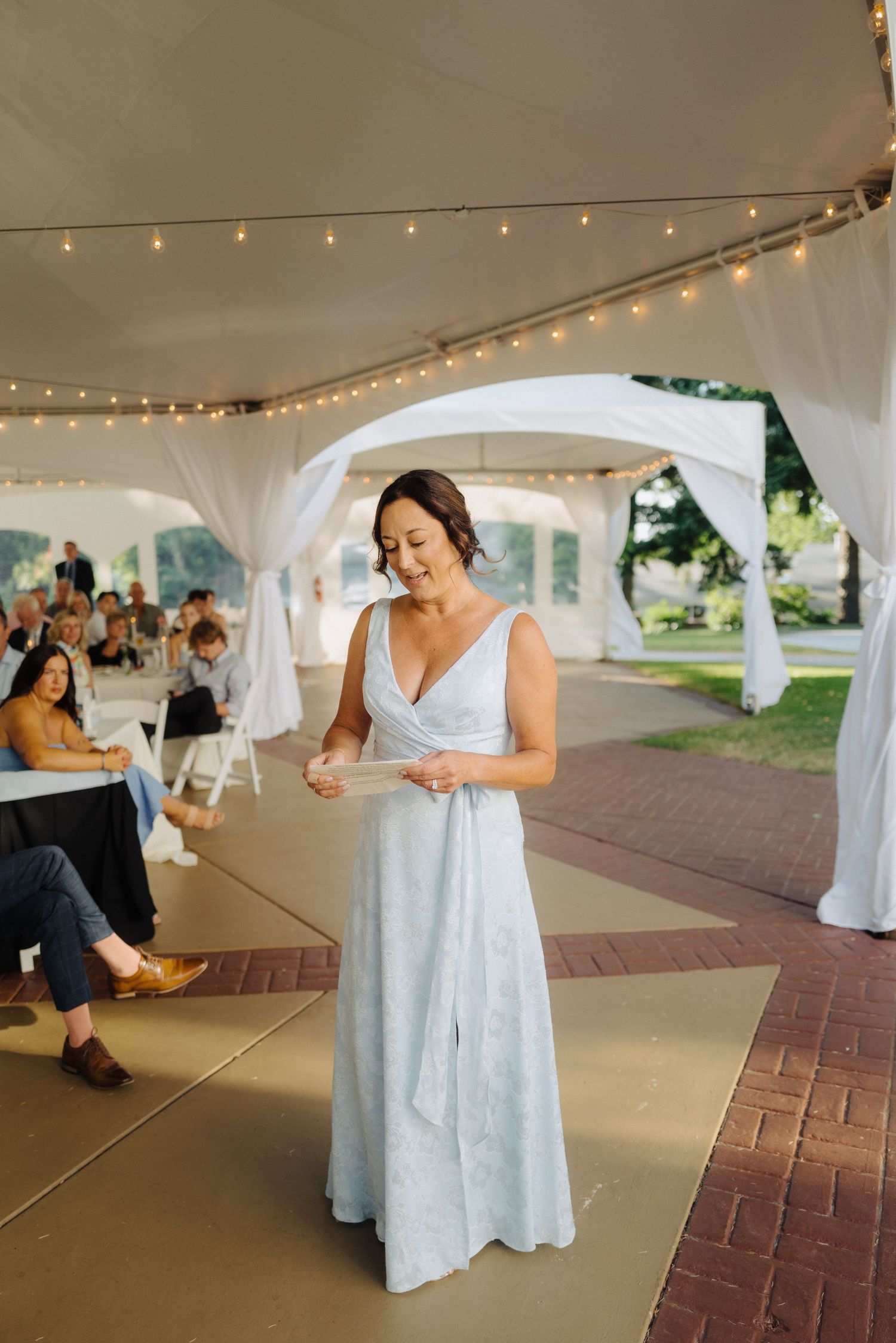 Dancing figures twirl under a white tent with string lights during an outdoor celebration.