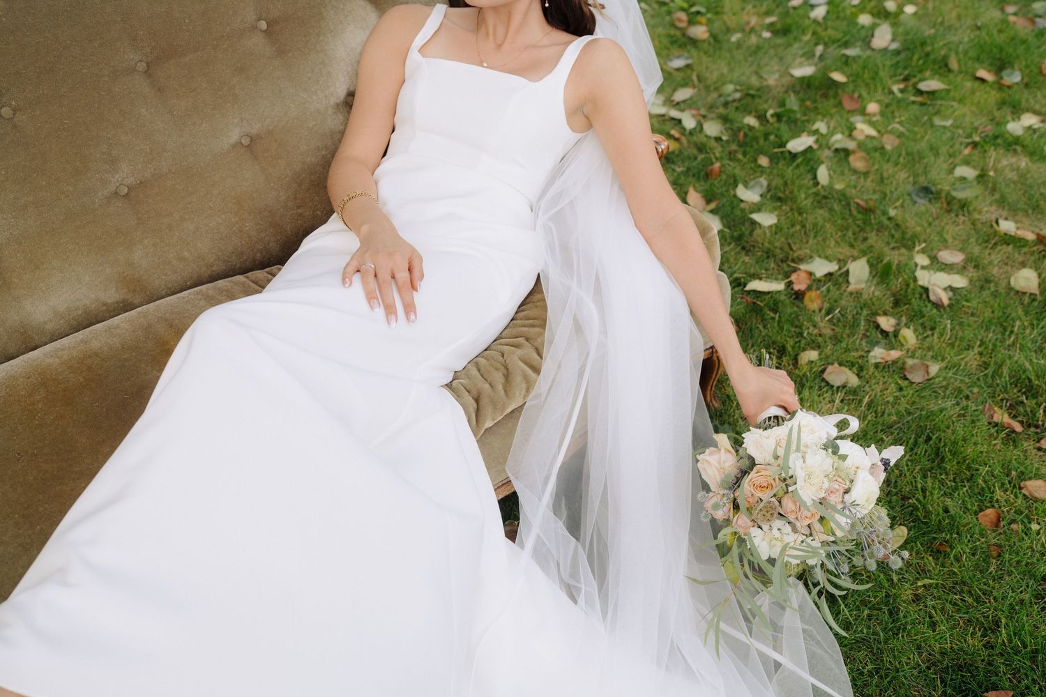 Wedding dress details shown on grass with delicate lace and flowing fabric in natural outdoor lighting.
