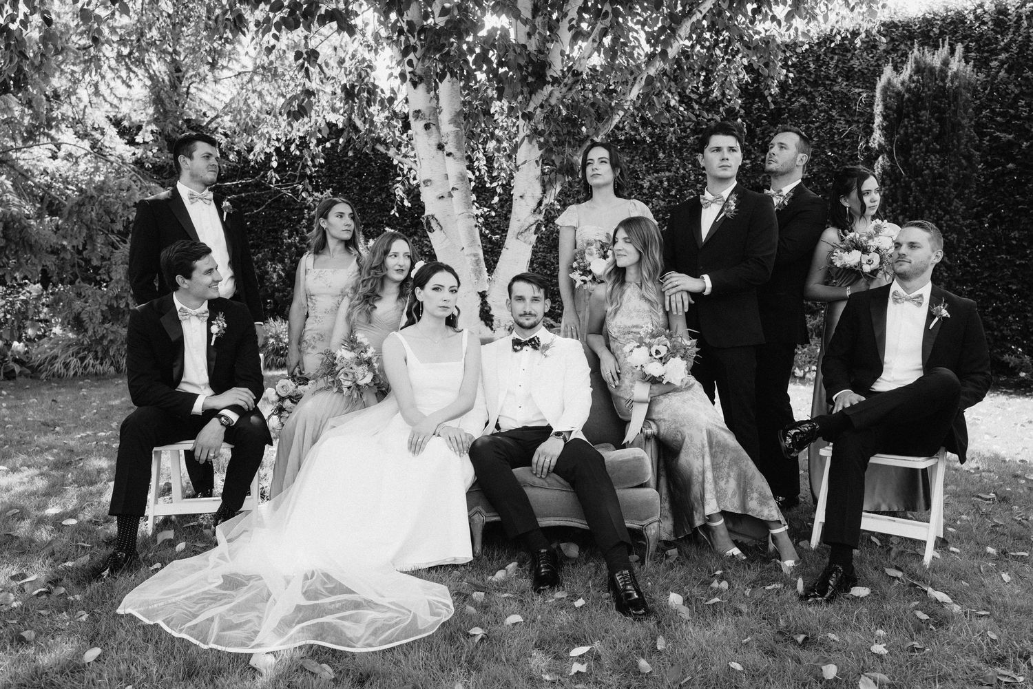 Wedding party in formal attire poses together outdoors in a black and white photograph.