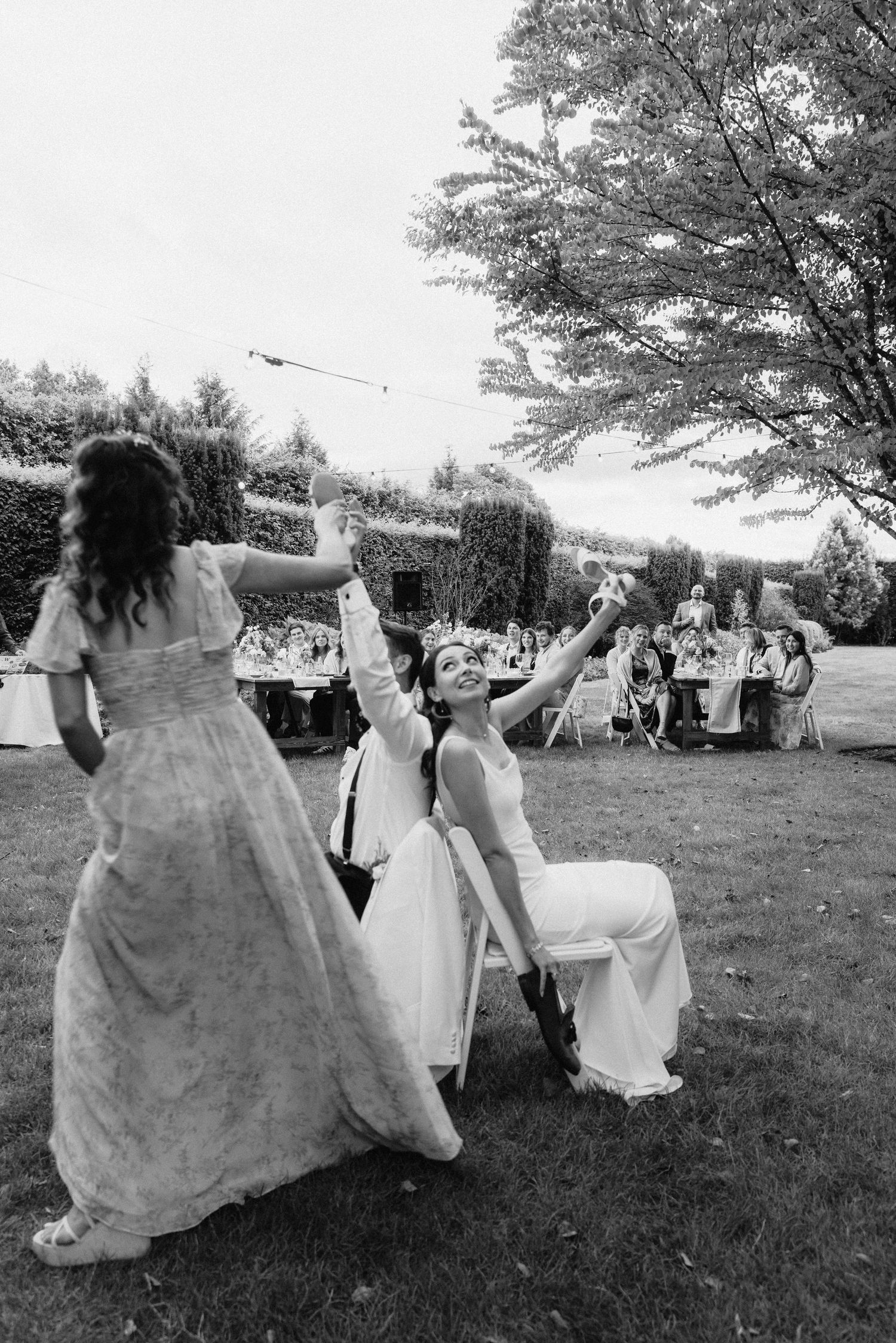 Black and white photo of wedding guests playing a fun outdoor game with white fabric.
