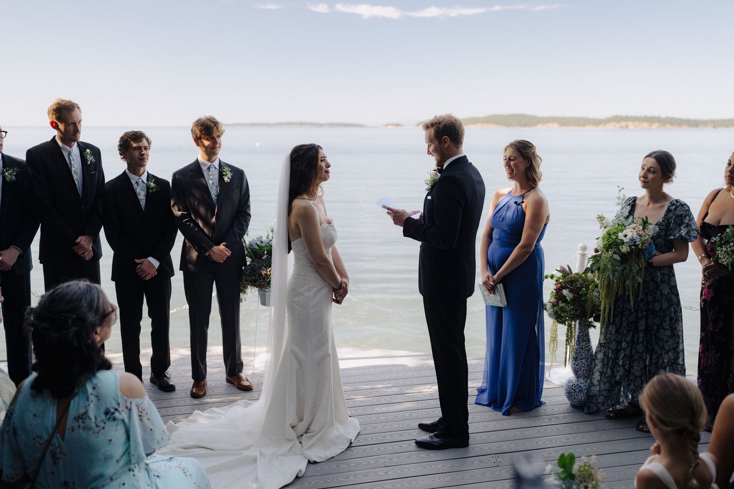 Oceanside wedding ceremony taking place on a wooden deck with stunning water views in the background.