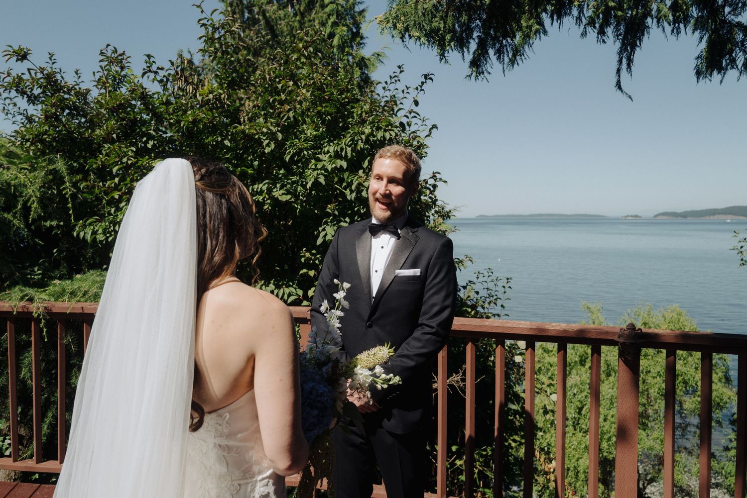 Outdoor wedding ceremony overlooking a scenic waterfront with trees and natural landscaping.