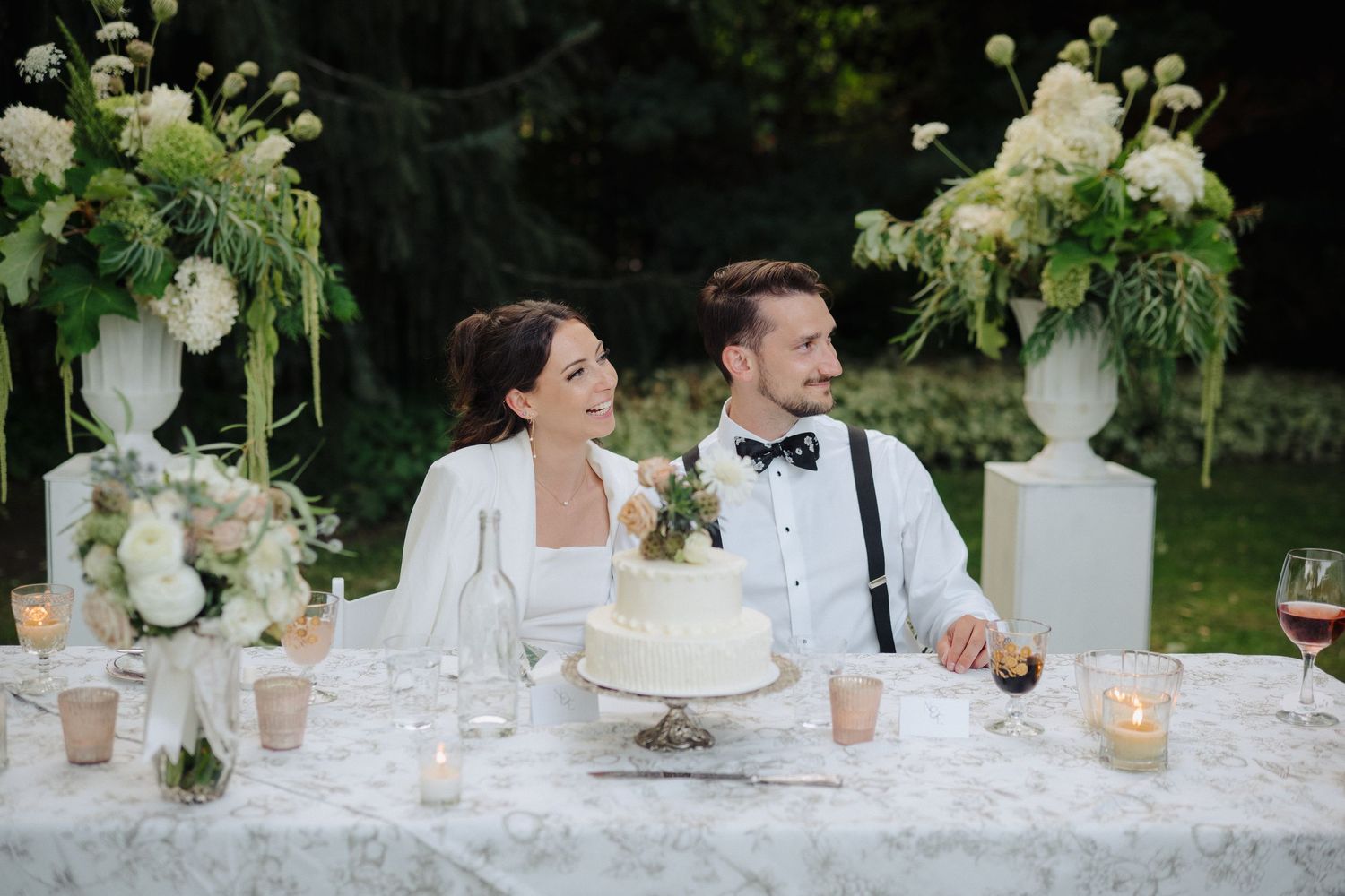 Elegant white wedding reception table with floral centerpieces and candles.