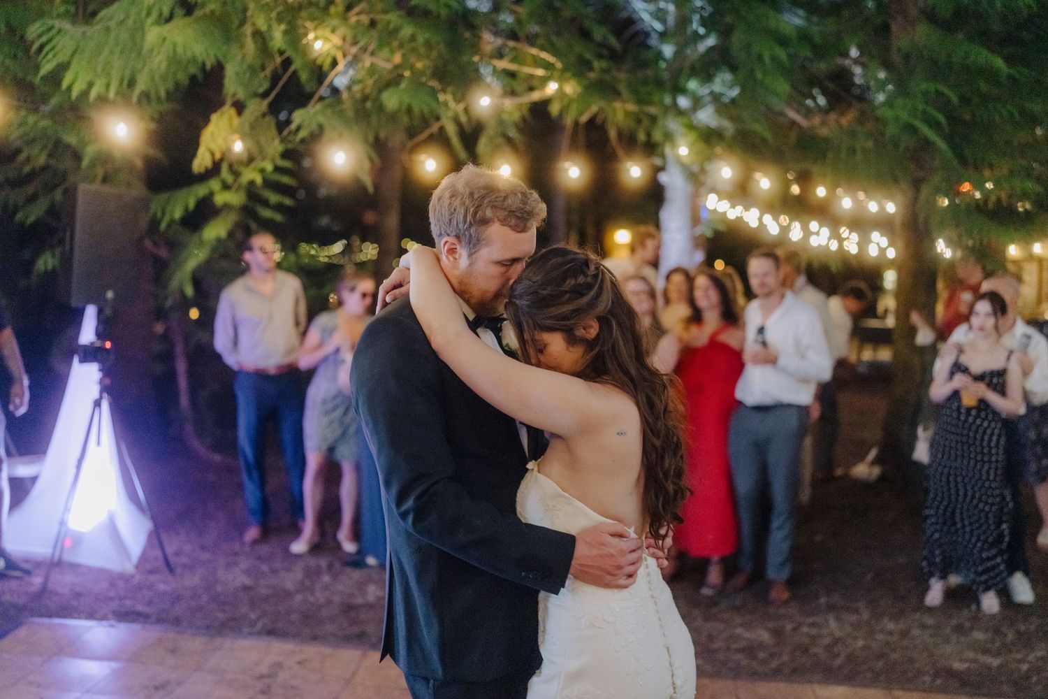 Outdoor evening wedding reception with string lights hanging among trees creating magical ambiance.