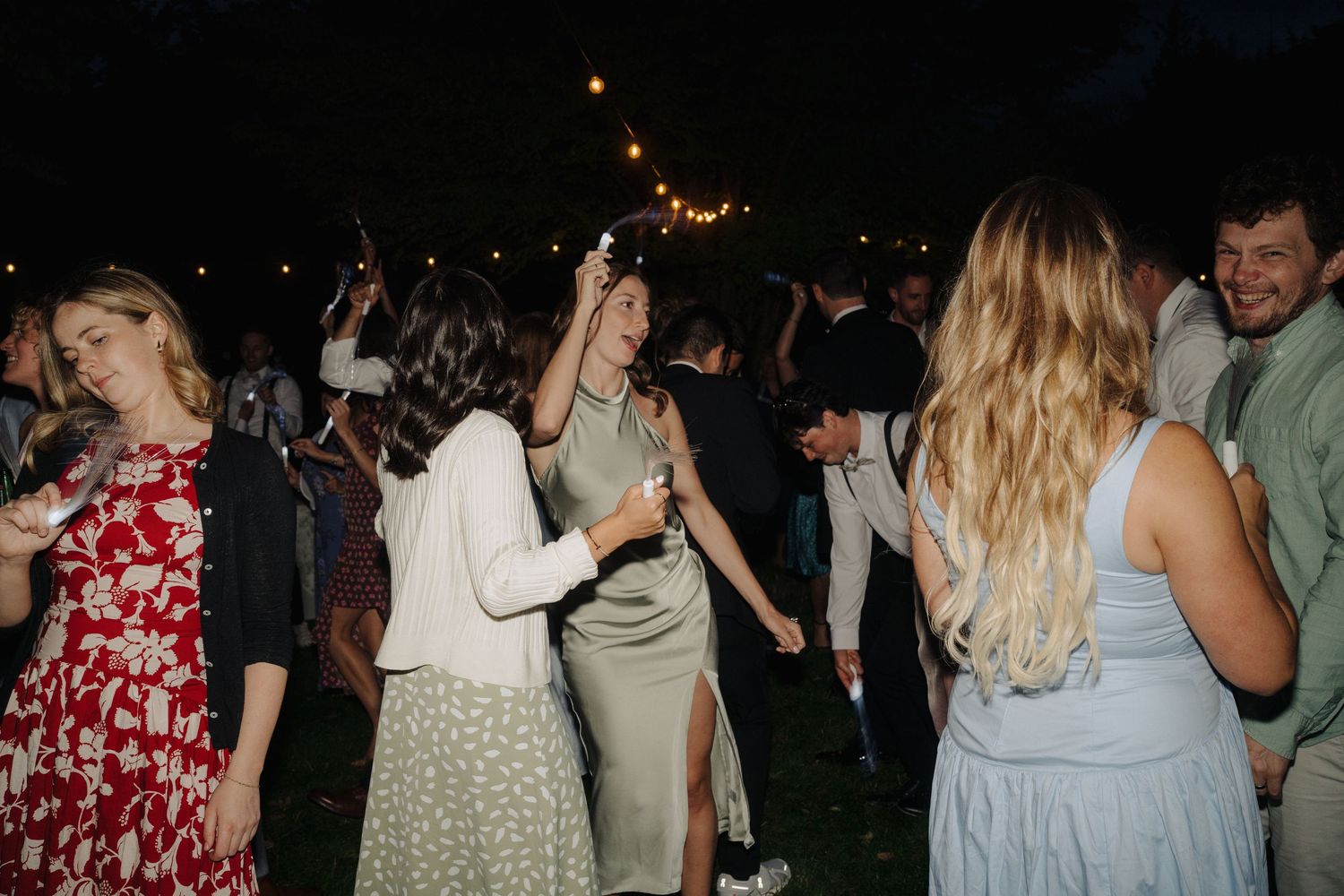 Wedding reception guests dance under evening lights at outdoor celebration.