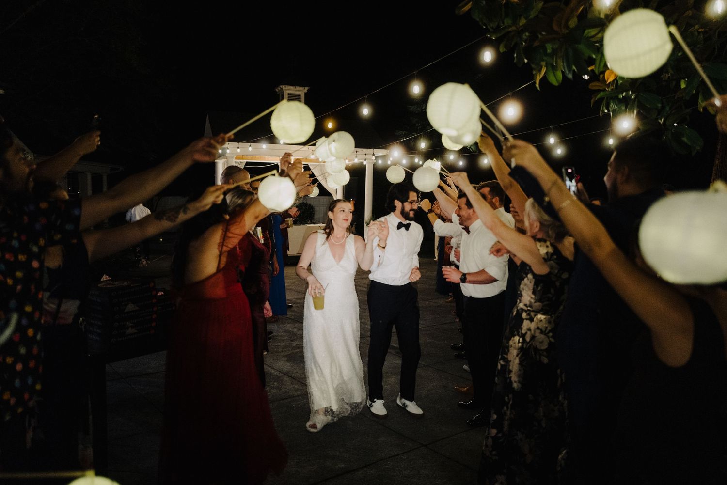 Wedding guests dancing under paper lanterns at an outdoor nighttime reception.