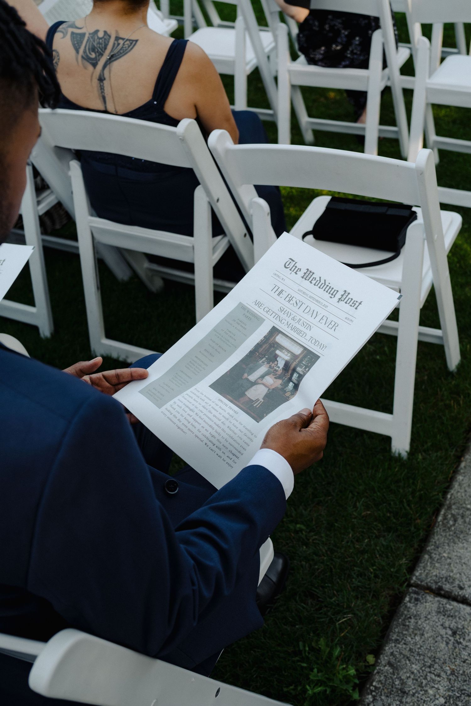 A guest reads through a wedding program while seated in white chairs at an outdoor ceremony.