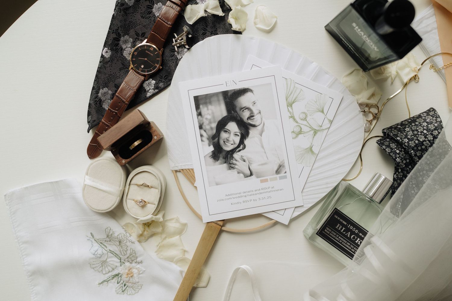 Flatlay of wedding details including rings, flowers, and stationery in neutral tones on white background.
