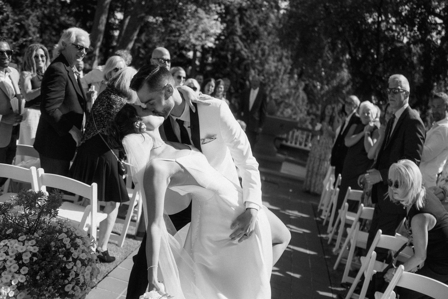Black and white photo of wedding ceremony guests seated in rows outdoors.