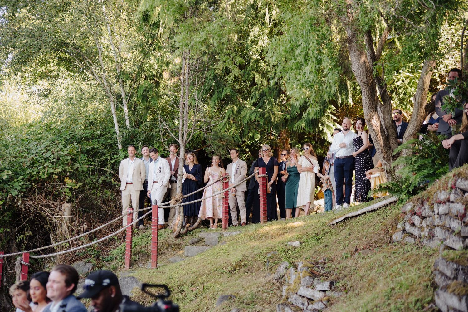 Wedding guests gathered along a tree-lined path for an outdoor ceremony.