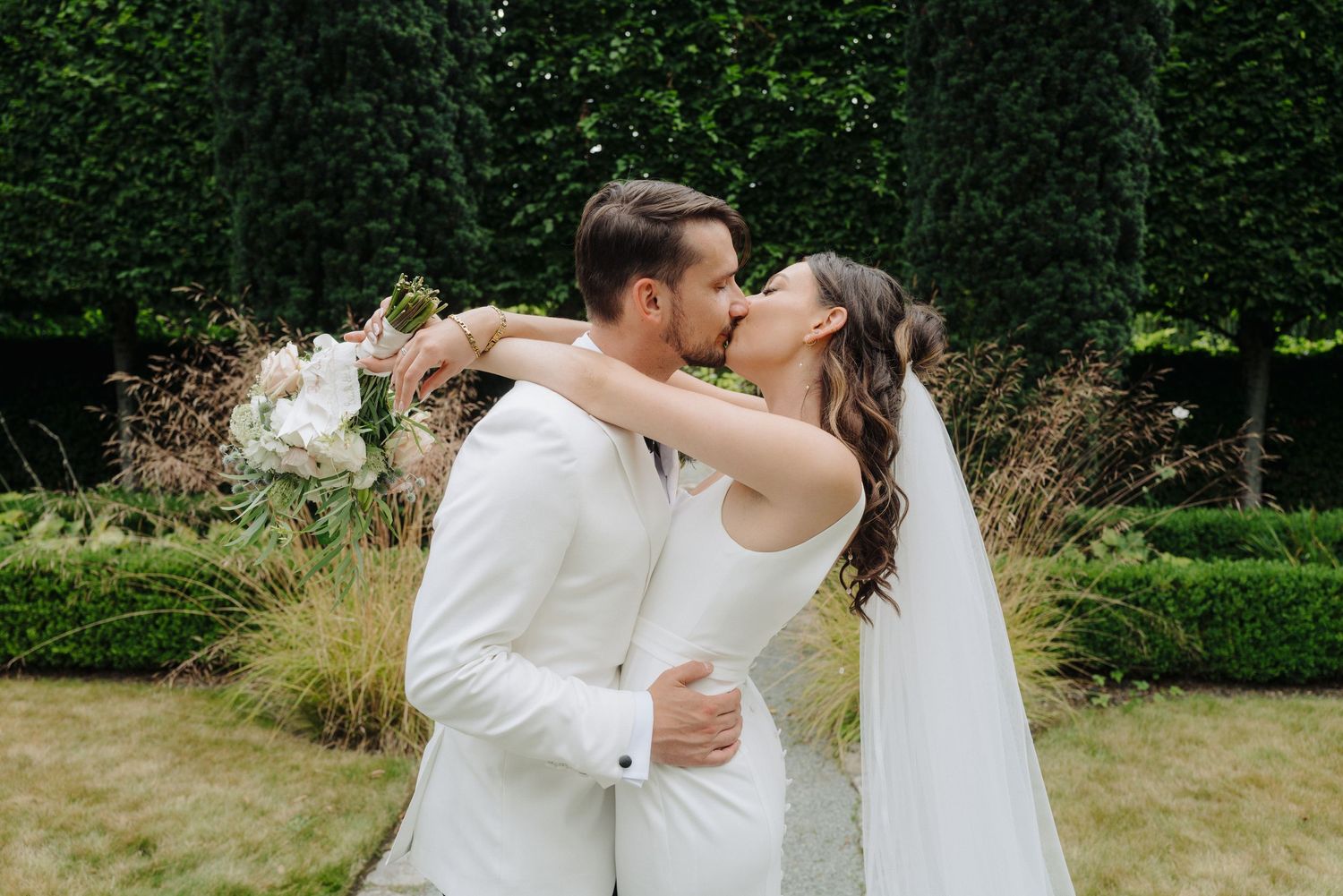 Romantic garden wedding portraits among green hedges and natural scenery.