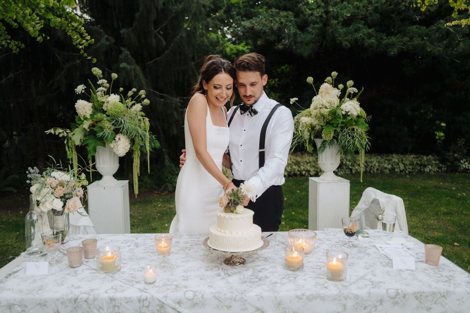 Elegant white wedding cake display with floral decorations and candles on a textured tablecloth.