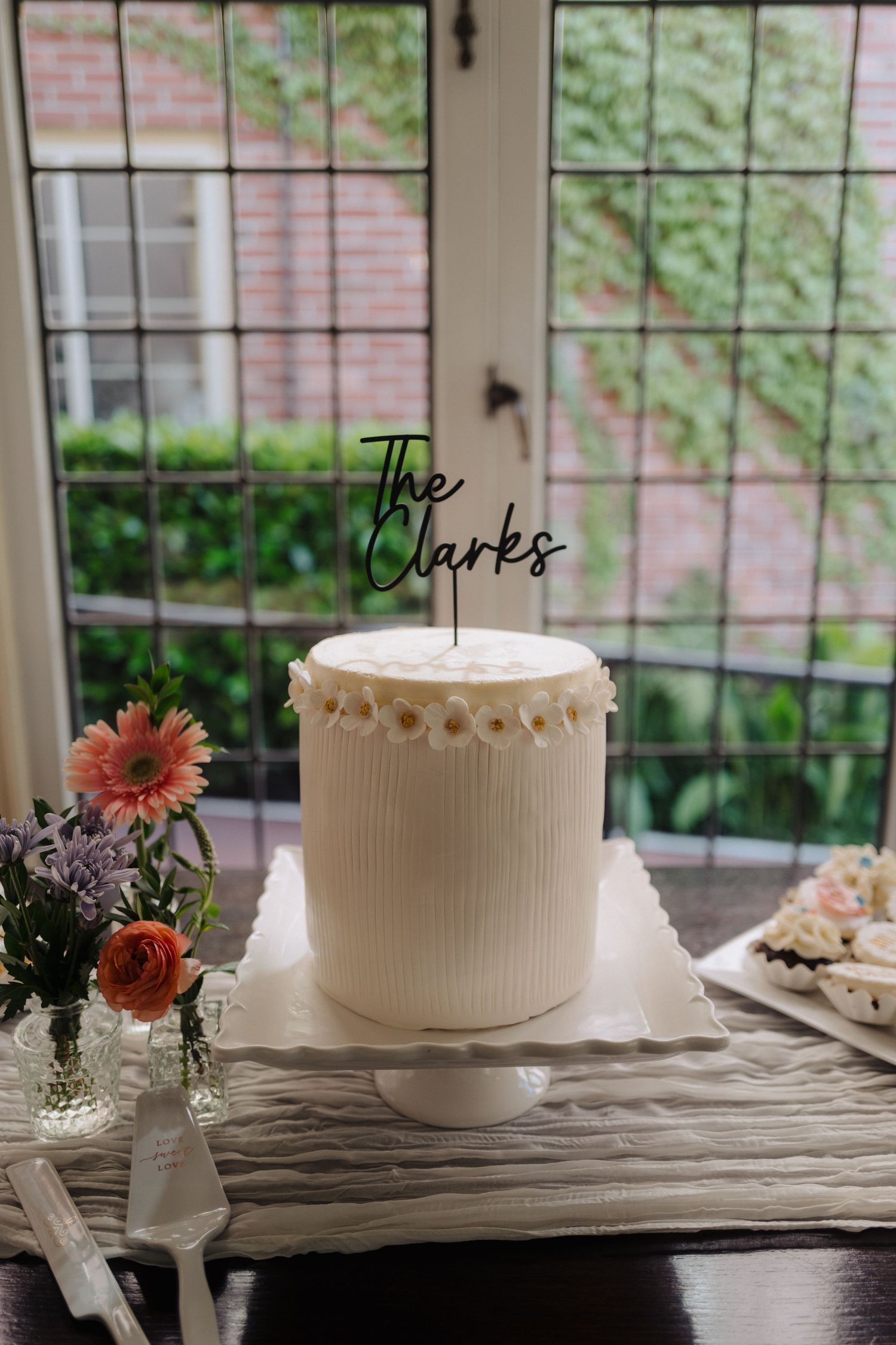 Simple white wedding cake displayed on rustic wooden table with floral decorations.