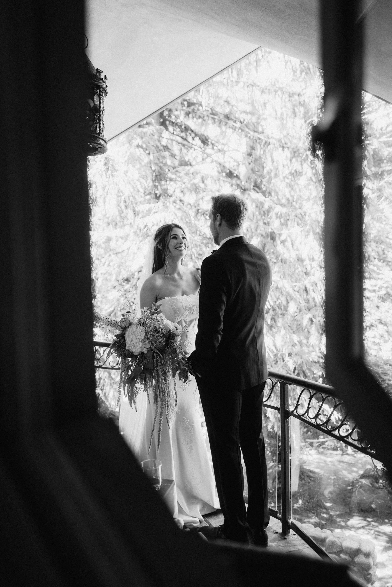Black and white romantic portrait of couple on balcony framed by architectural elements.