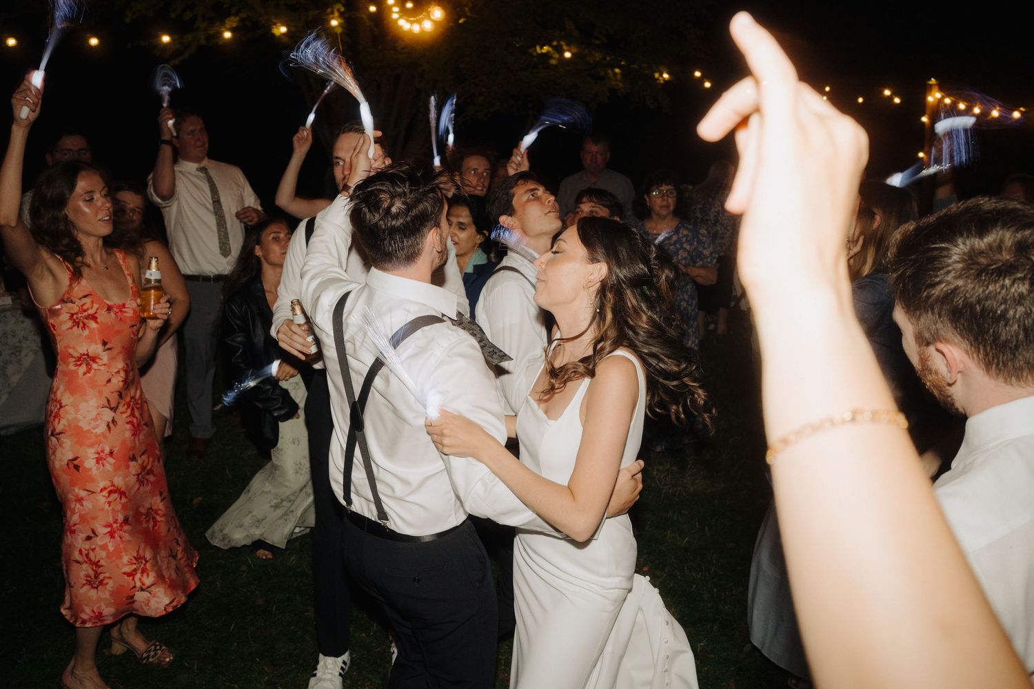 Wedding reception dance party with guests celebrating under twinkling lights at night.