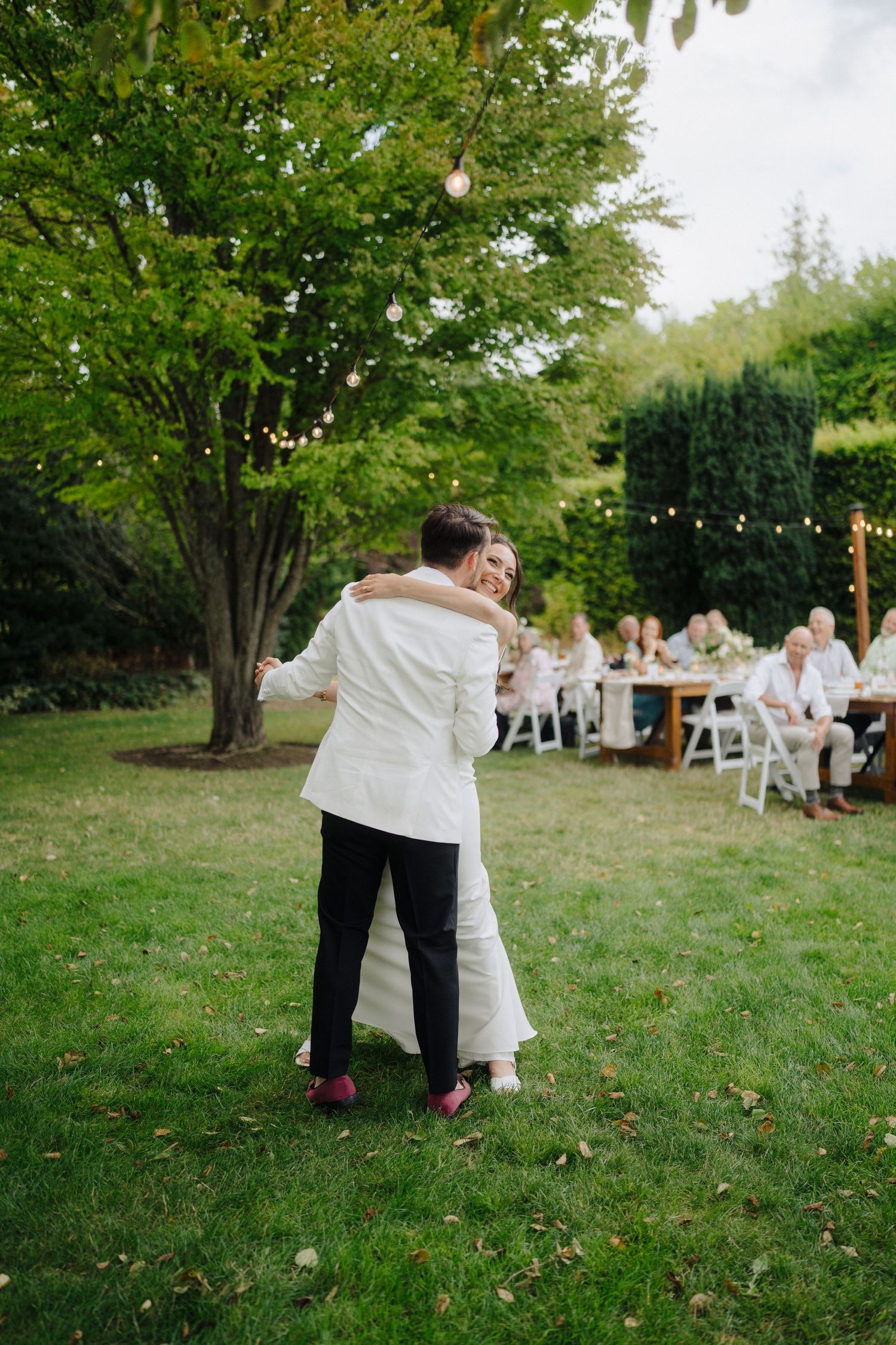 Wedding guests seated at outdoor tables with string lights and trees in the background.
