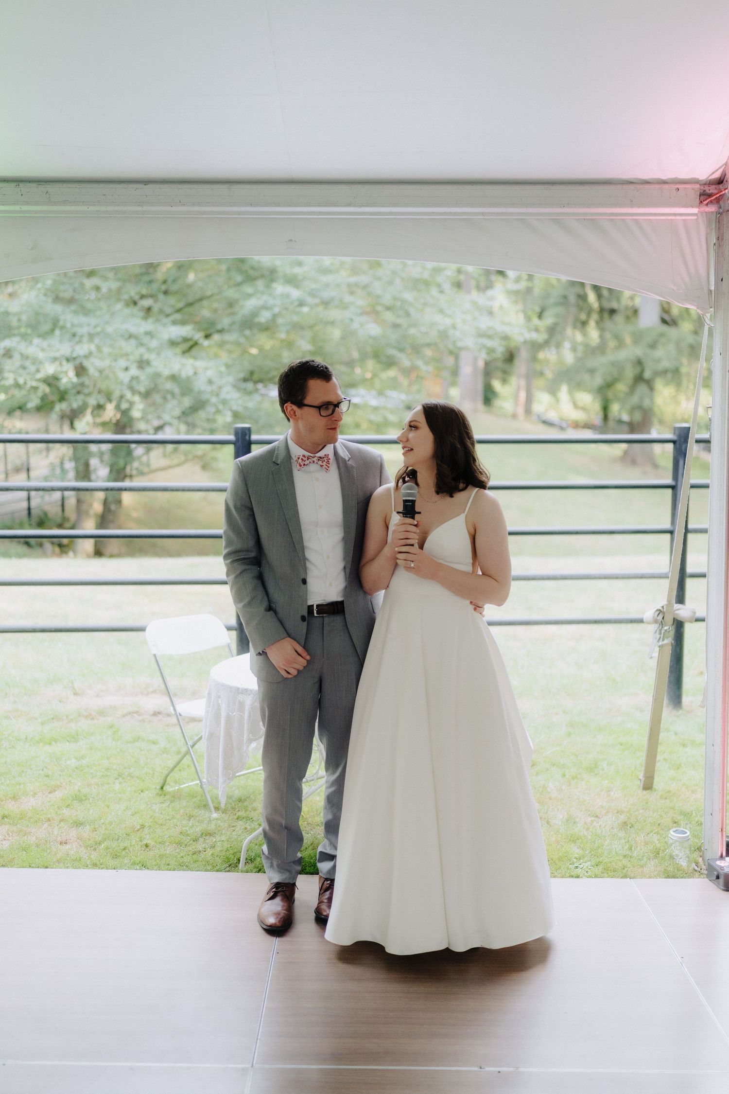 A bride and groom share a tender moment under a covered outdoor venue with rustic railings.